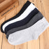 Multiple cotton crew socks in black, white, dark blue, and gray, arranged on wooden surface