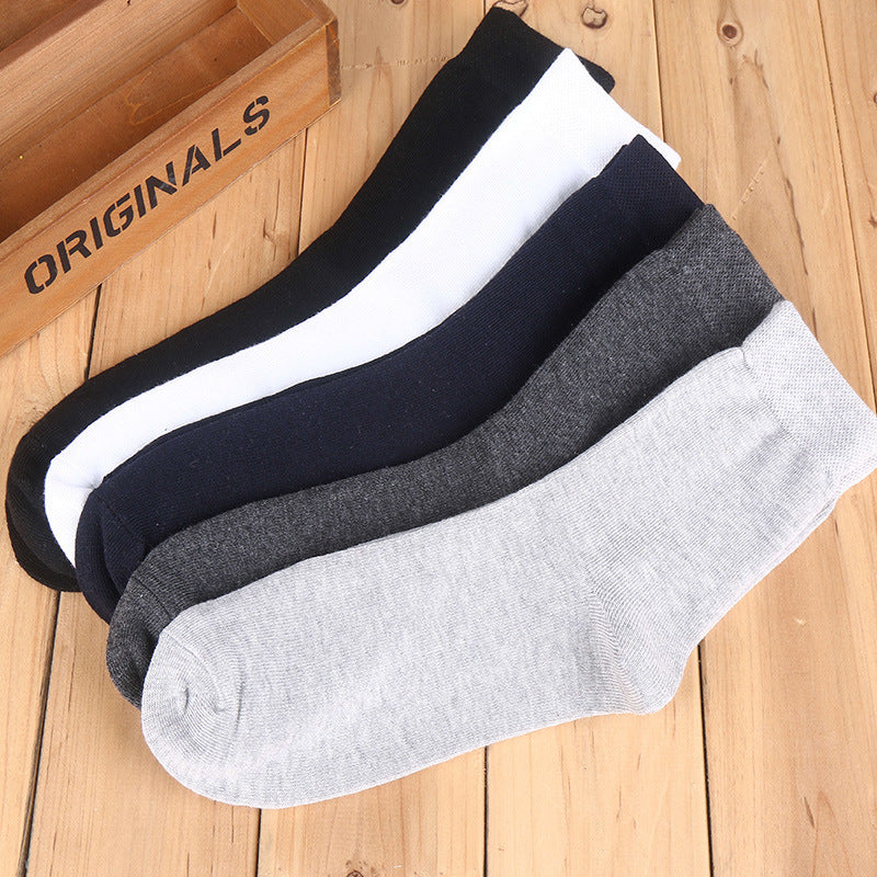 Multiple cotton crew socks in black, white, dark blue, and gray, arranged on wooden surface