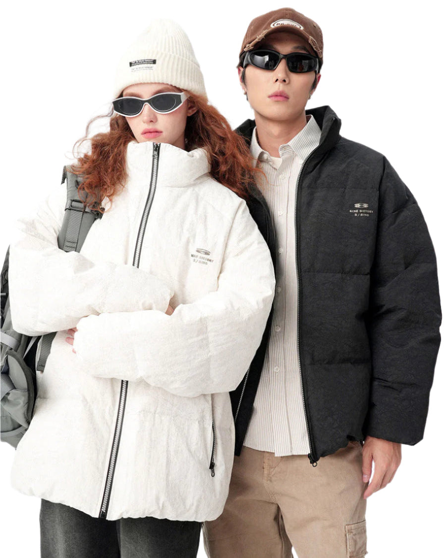 Models wearing matching puffer jackets - woman in white with beanie and man in black with cap, both with sunglasses against white background