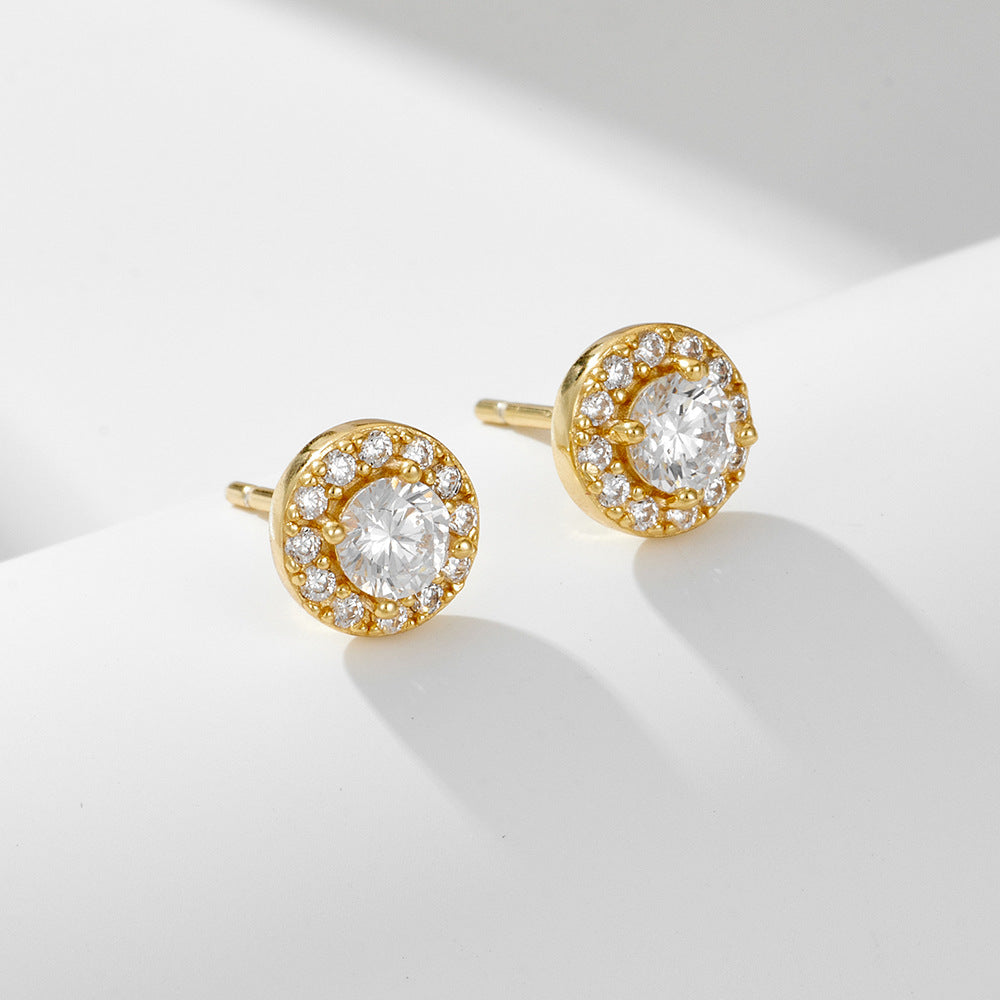 A pair of gold stud earrings featuring round center diamonds surrounded by diamond halos displayed against white backdrop