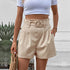 Front view of beige belted shorts with pleated waist detail and tropical plant decor