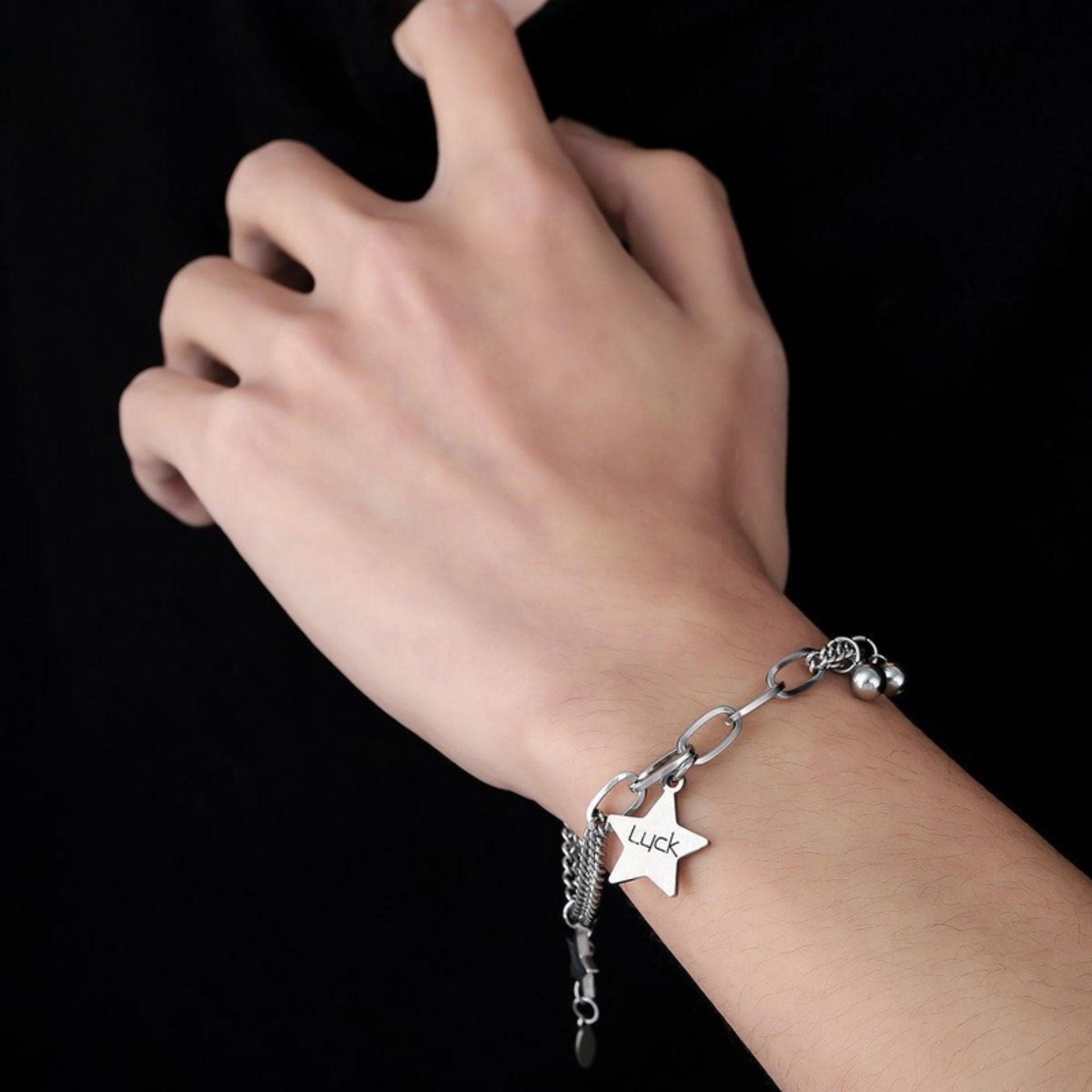 A close-up of a person's wrist wearing a silver chain bracelet with a star charm engraved with the word "Luck," along with small silver beads.