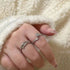 A person wearing silver twig and rose rings on their fingers, resting hand against white fluffy fabric, showcasing the nature-inspired design