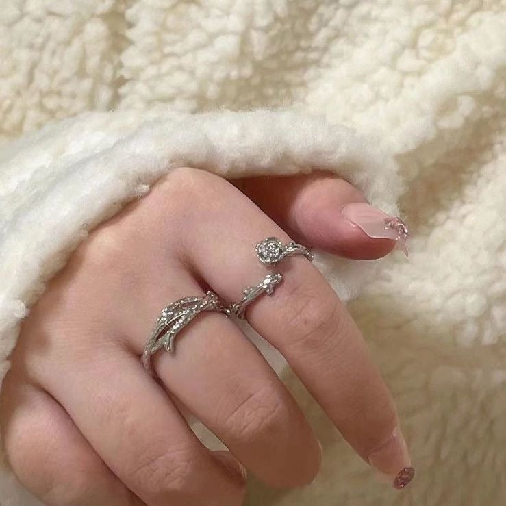 A person wearing silver twig and rose rings on their fingers, resting hand against white fluffy fabric, showcasing the nature-inspired design