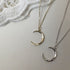 Close-up of silver and gold crescent moon pendants with detailed chain design against lace backdrop