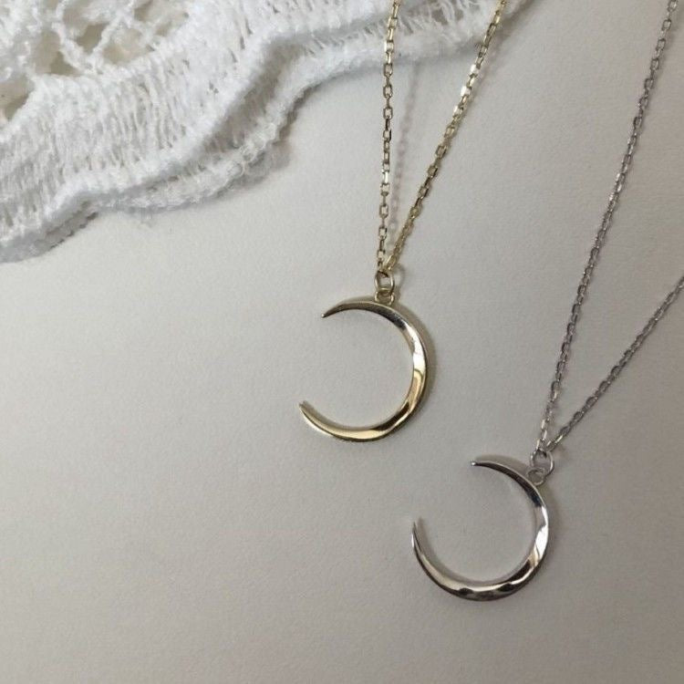 Close-up of silver and gold crescent moon pendants with detailed chain design against lace backdrop