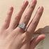 A woman wearing silver engagement ring with matching wedding band featuring baguette diamonds and cushion-cut center stone in sunlight