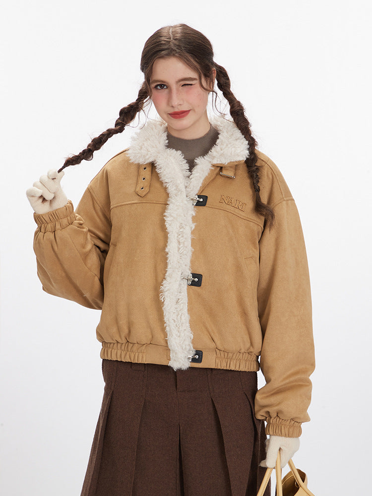 A woman wearing a tan shearling bomber jacket with white fleece lining, braided hair, and brown pleated skirt posing against white background