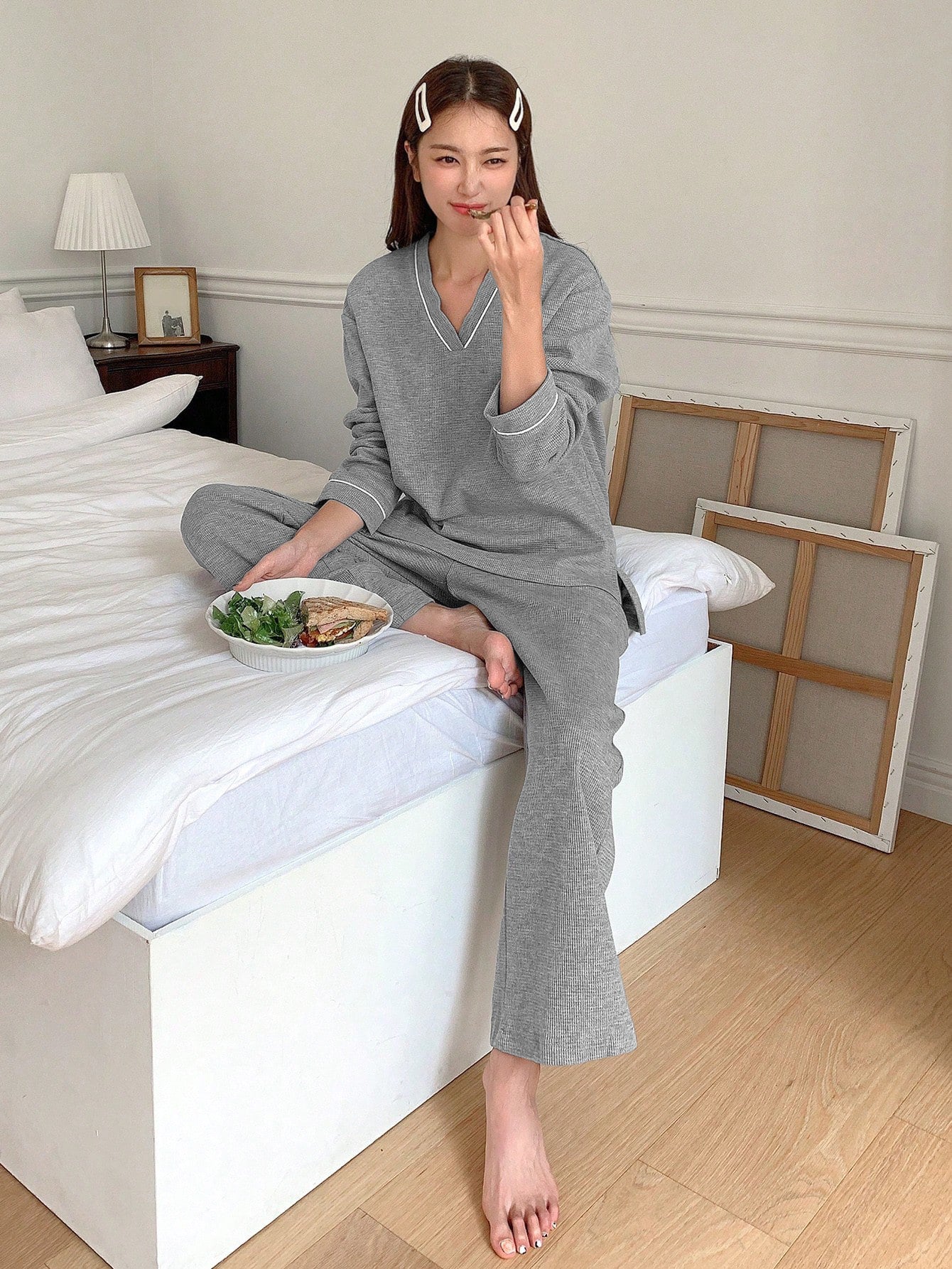 Model on bed wearing gray loungewear set while having lunch with salad and sandwich
