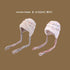 Close-up of white fuzzy winter hats with colorful speckles and multicolored braided earflaps against brown background