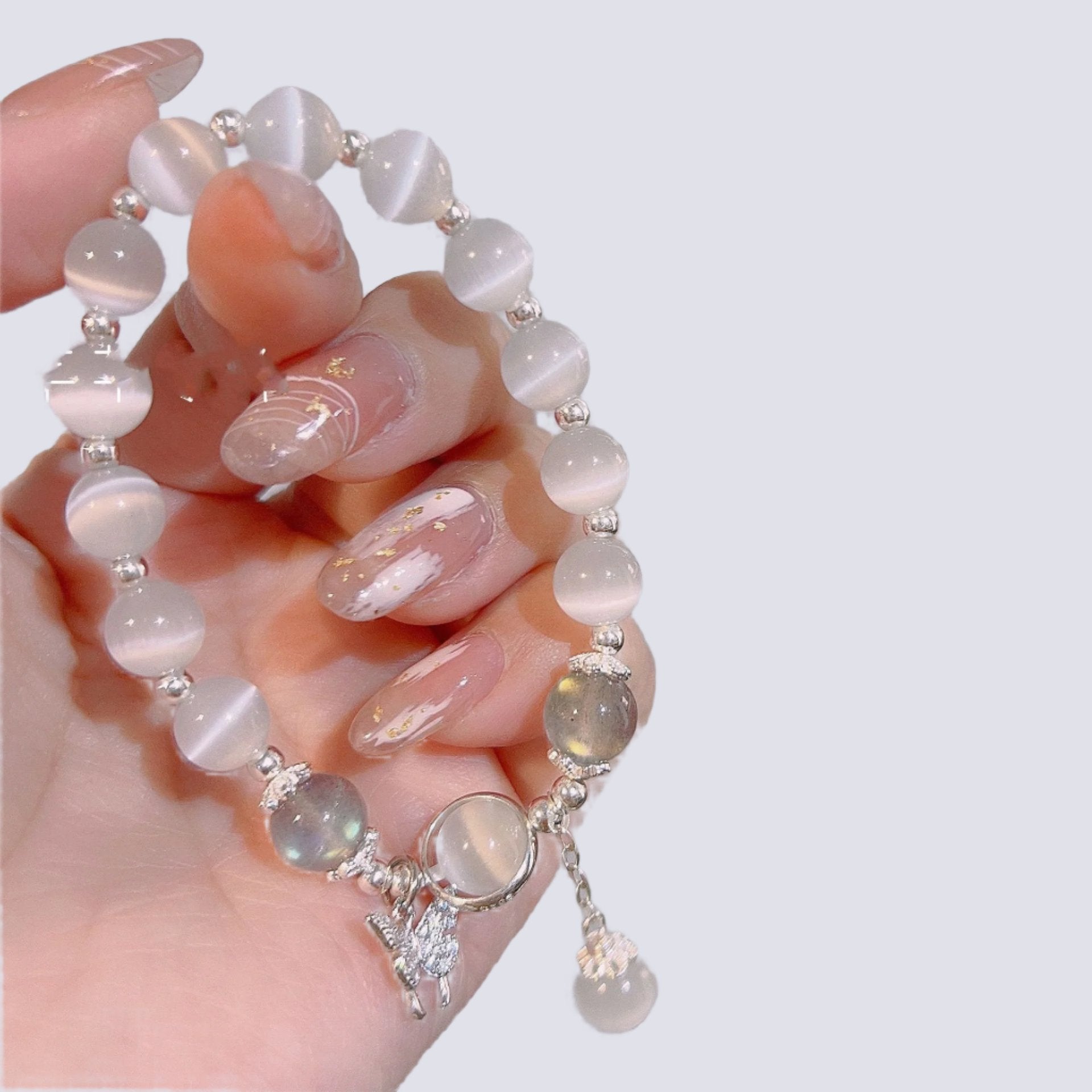Elegant blue cat's eye beaded bracelet with crystal butterfly pendant, held against pale skin with glossy manicure
