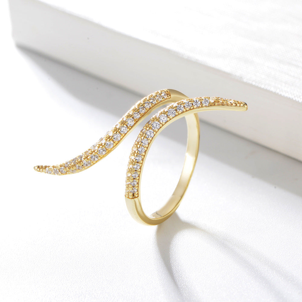 Gold-toned wave ring with crystal pavé, displayed against white surface with dramatic shadow