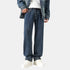 A model is wearing dark blue wide-leg jeans with a denim jacket and white top, standing against a white background