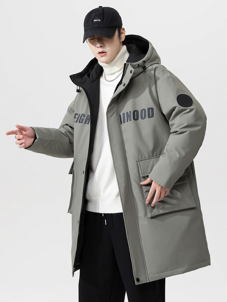 A man wearing a gray-green NEIGHBORHOOD parka poses with white turtleneck and black baseball cap against white background
