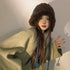 Brown furry winter hat with blue braided ties, modeled with sage green oversized sweater