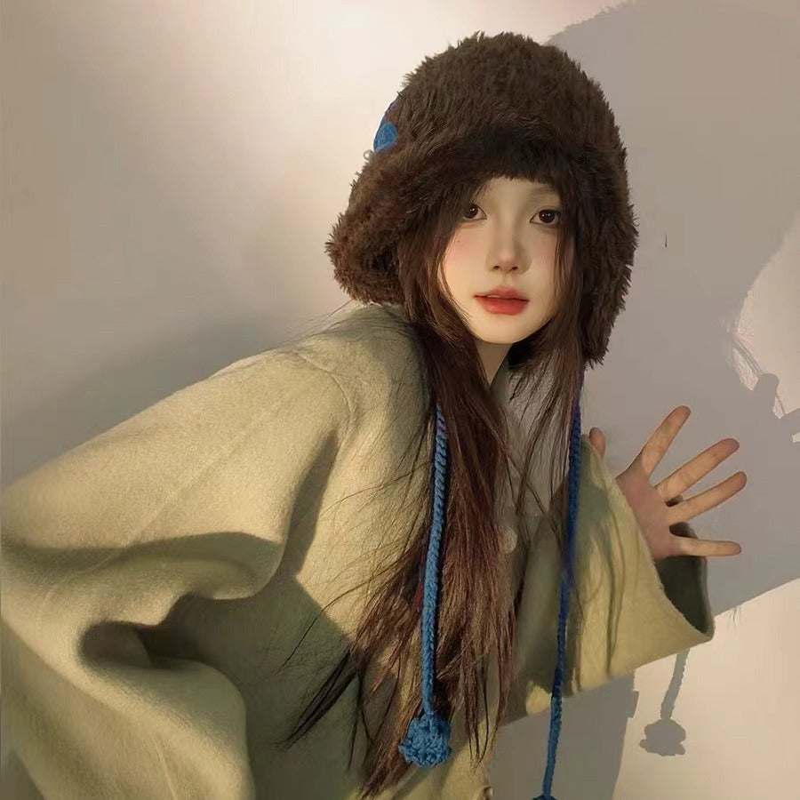 Brown furry winter hat with blue braided ties, modeled with sage green oversized sweater