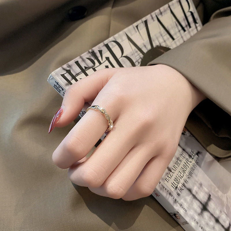 Hand wearing delicate gold twisted ring with crystals, resting on book or magazine