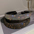 Wide black headband fully covered in iridescent rhinestones, reflecting light for a dazzling effect, placed on a glossy surface.