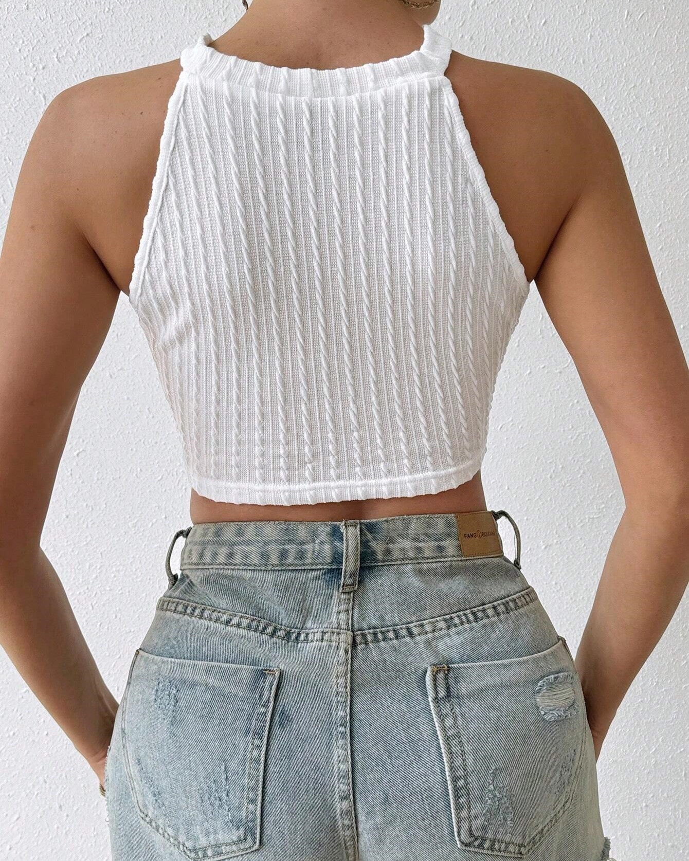 Back view of white ribbed knit halter crop top paired with distressed denim shorts.