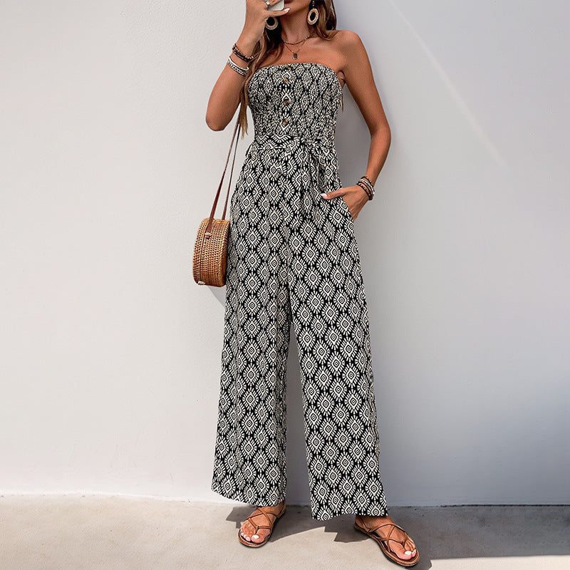 Woman wearing a black and white geometric strapless jumpsuit with a tie waist, holding a woven handbag while taking a mirror selfie.