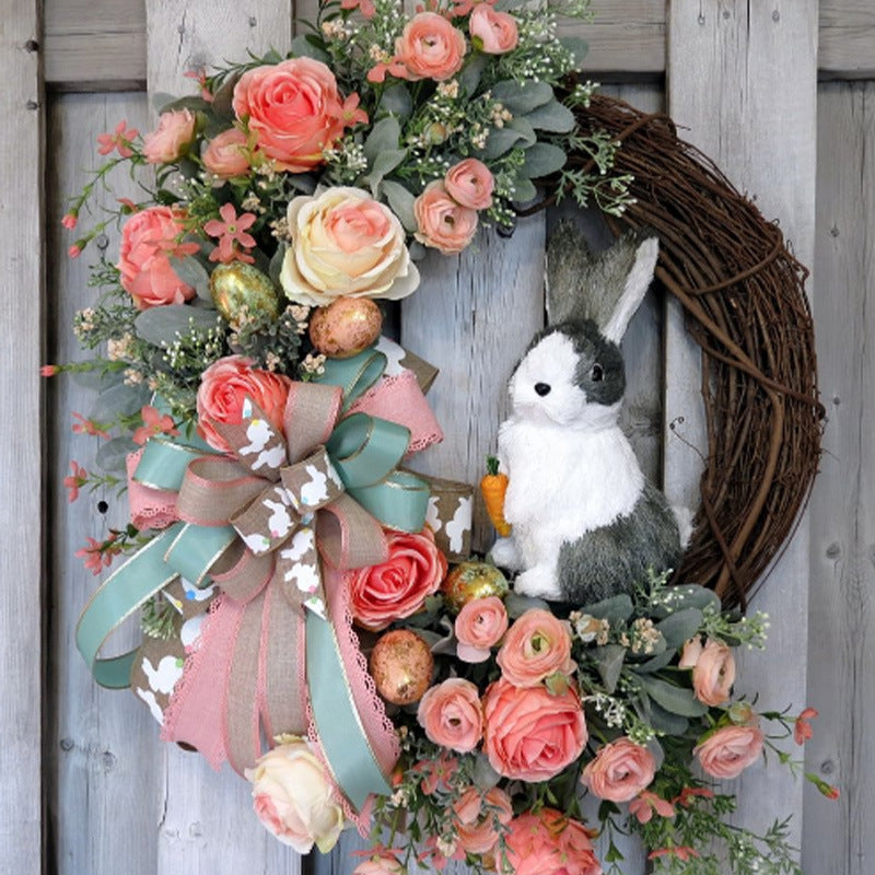 A pastel floral wreath with pink and cream roses, a burlap bow, and a plush bunny holding a carrot, perfect for Easter decor.