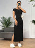 Front view of woman in fitted black maxi dress with side slit, holding small white bag and wearing silver accessories