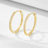 Gold pave diamond hoop earrings displayed on white surface. Delicate hinged hoops feature sparkling crystals along the outer rim with secure closures