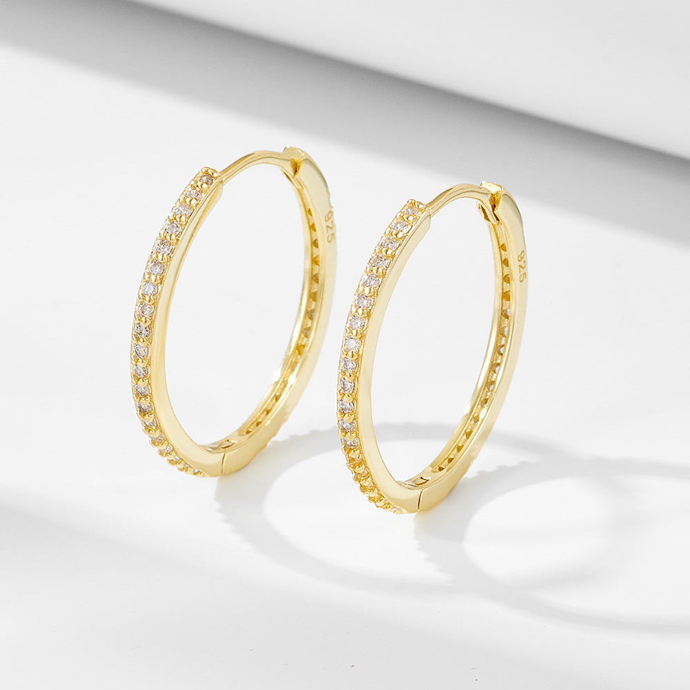 Gold pave diamond hoop earrings displayed on white surface. Delicate hinged hoops feature sparkling crystals along the outer rim with secure closures