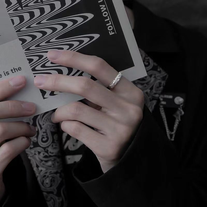 Close-up of engraved silver ring worn on hand holding book, showing detailed pattern in moody lighting