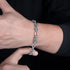 Close-up of a man’s wrist wearing a silver rope-style chain bracelet, with his thumb pointing up, against a black background.