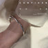 A model is wearing a silver wavy bangle bracelet on their wrist against cream silk fabric with inspirational text overlay that reads 'CONFIDENCE' and a quote about faith