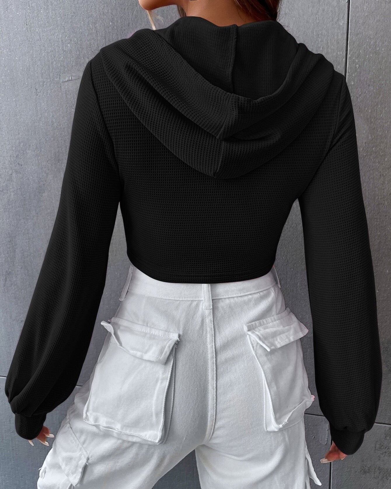 Back view of black textured crop hoodie showing fitted silhouette with balloon sleeves and white cargo pants