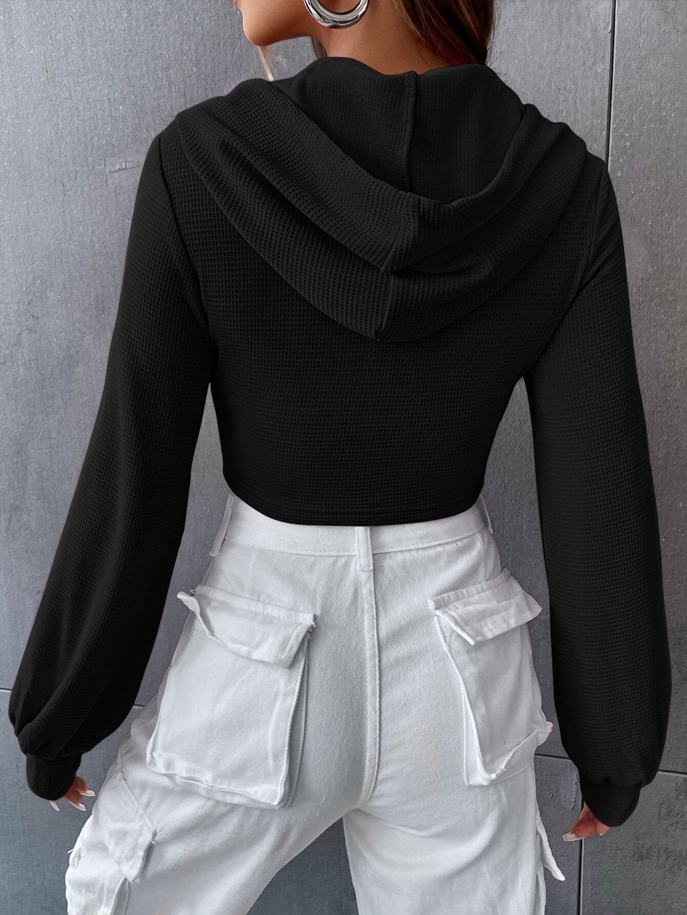 Back view of black textured crop hoodie showing fitted silhouette with balloon sleeves and white cargo pants