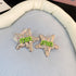 Silver star-shaped hair clips with a textured metallic finish and green "min" lettering, displayed on soft fabric.