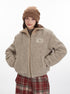 Model wearing beige teddy fleece jacket with Marule patch, brown beanie and red plaid pants. Cozy winter style against white backdrop
