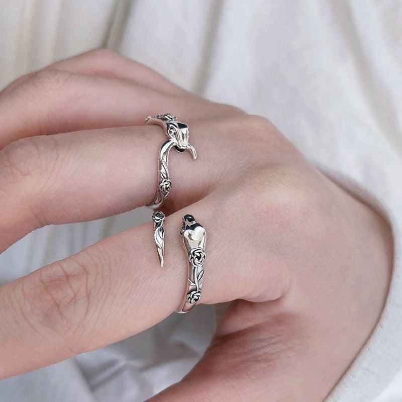 A model is wearing a silver snake ring on their finger against white fabric. The open band displays floral detailing