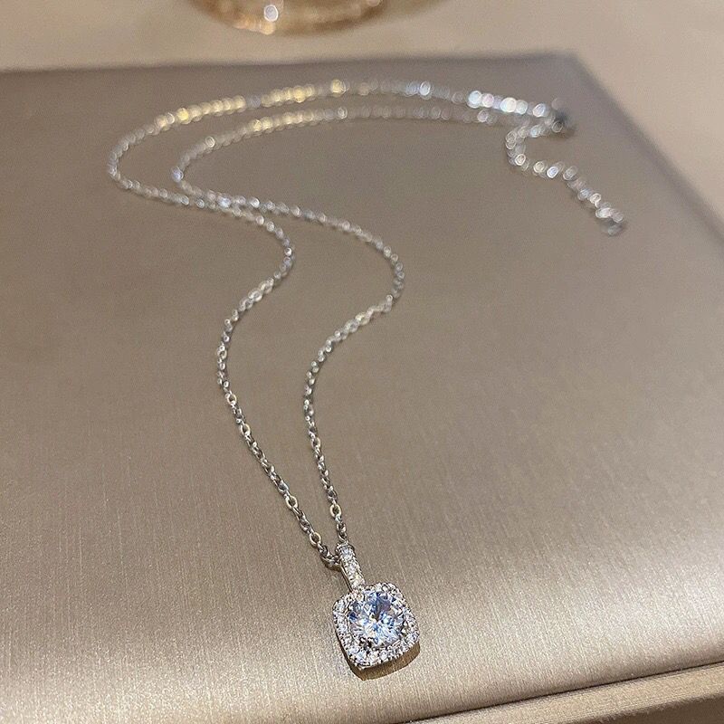 Sterling silver necklace with blue crystal pendant and square halo setting displayed on metallic surface with sparkle effect
