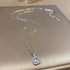 Sterling silver necklace with blue crystal pendant and square halo setting displayed on metallic surface with sparkle effect