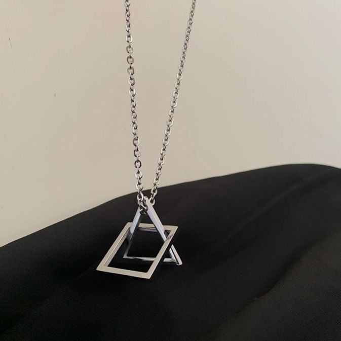 Silver geometric pendant necklace with overlapping square and triangle charms, displayed against a black fabric background