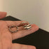 A person holding three silver rings in their palm - a Roman numeral ring, braided chain ring, and layered band ring against a neutral background