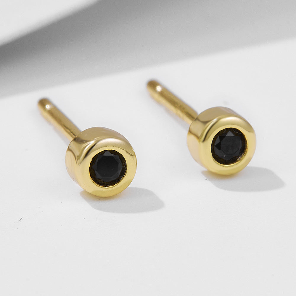 Close-up of gold-plated round stud earrings with black nano zirconia stones on white surface