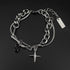 Men’s layered chain bracelet in stainless steel with a cross pendant and black gemstone charm, displayed on a black surface.