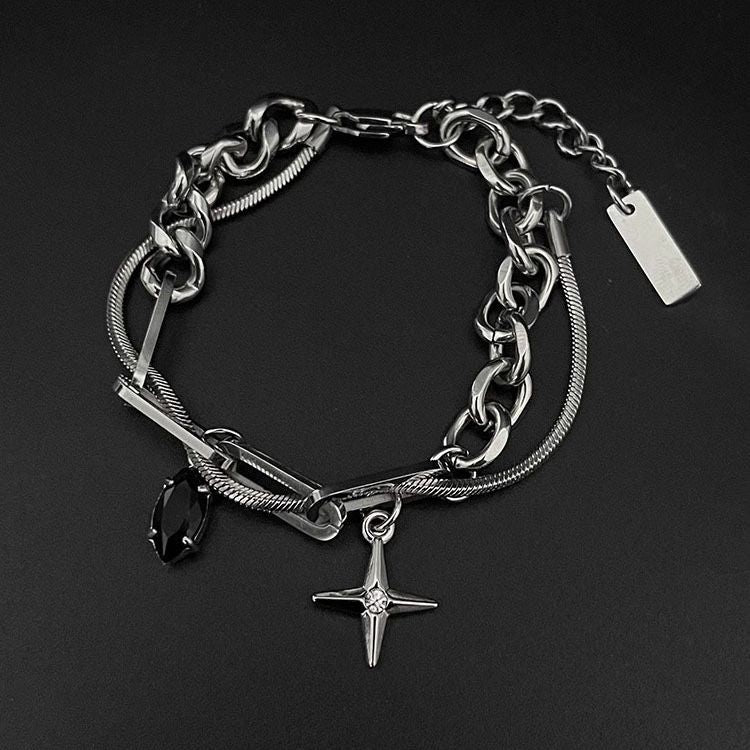 Men’s layered chain bracelet in stainless steel with a cross pendant and black gemstone charm, displayed on a black surface.