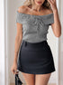  Woman in a gray off-shoulder ribbed top with a tie detail, paired with a black mini skirt, holding a small black handbag.