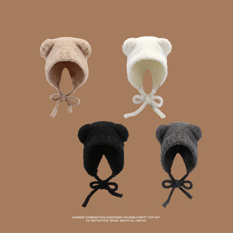 Four plush teddy bear ear hats arranged on a brown background in beige, white, black, and gray colors, featuring soft fabric and chin ties