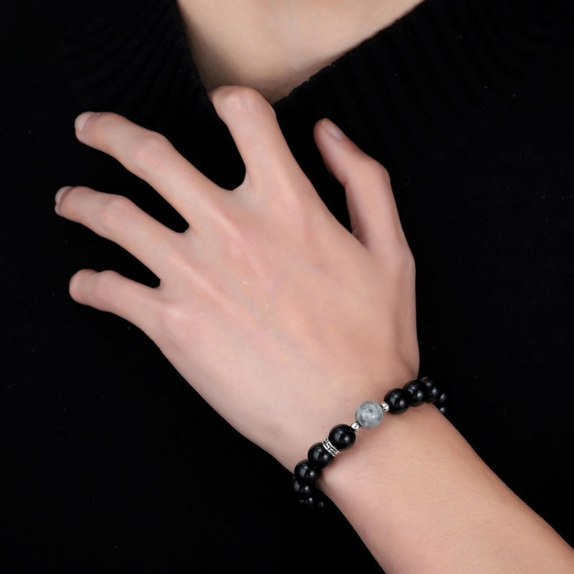 Close-up of a black beaded bracelet with a single marbled gray bead, worn on a wrist against a black background.