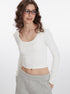 White long-sleeve crop top with scoop neckline and fitted silhouette, paired with light gray wide-leg pants with pockets