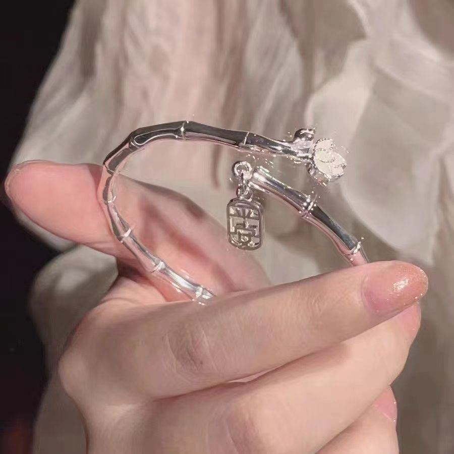 A silver bamboo bangle with lotus flower and Chinese symbol charm held in hand against soft fabric