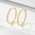 Gold diamond hoop earrings displayed on white minimalist surface. The elegant hoops feature pave-set crystals catching light with clear shadows