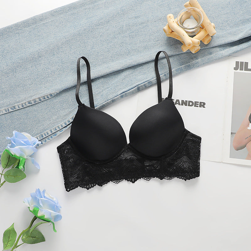 A black push-up bra with delicate lace trim displayed on white surface beside light denim fabric and blue roses. Wooden candle holder visible